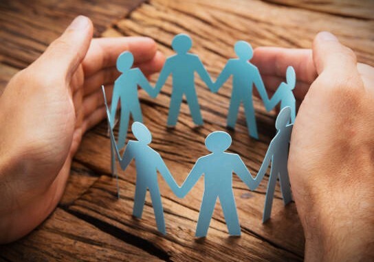 Cropped image of businessman's hands covering paper team on wooden table